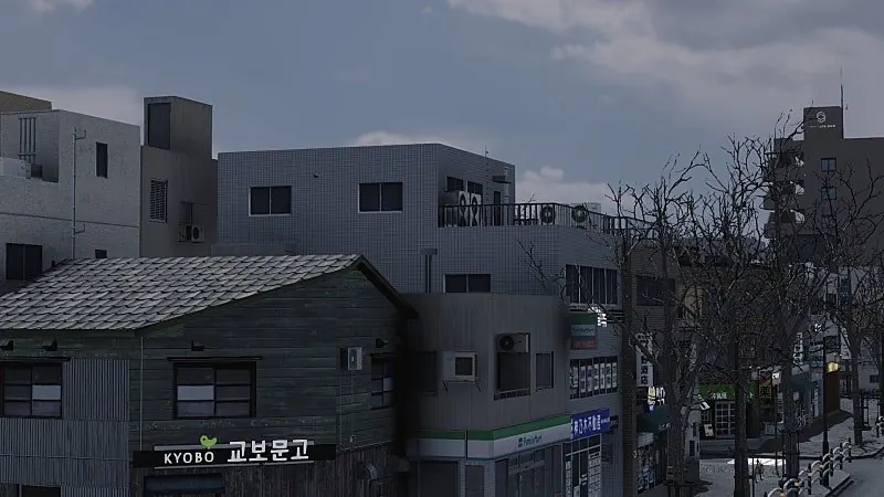 이른 겨울의 낮은 상가 골목. 초록 판자를 두른 목조 건물의 기와지붕에 눈이 얇게 앉았고, 옆 건물 1층에는 편의점이 들어서 있다.